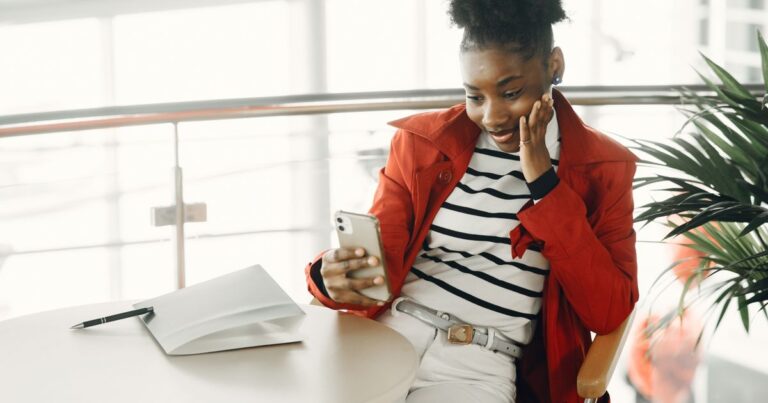 Jeune candidate en veste rouge découvrant sur son téléphone ce qu'une IA répond au sujet d'un employeur