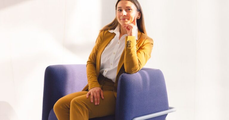 Process de recrutement vu du candidat : une candidate en tailleur jaune, assise sur un fauteuil bleu, attend son entretien dans un espace lumineux