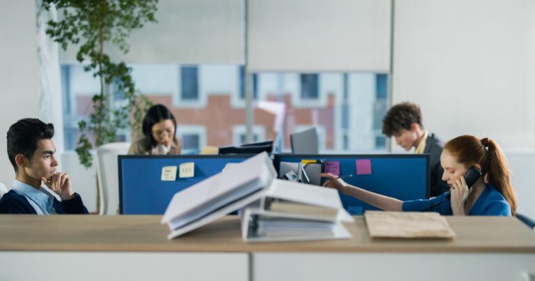 Entreprise archipel 2026 : quatre salaries travaillant isolement dans des bureaux cloisonnes, illustration de la fragmentation du collectif et de son impact sur la marque employeur