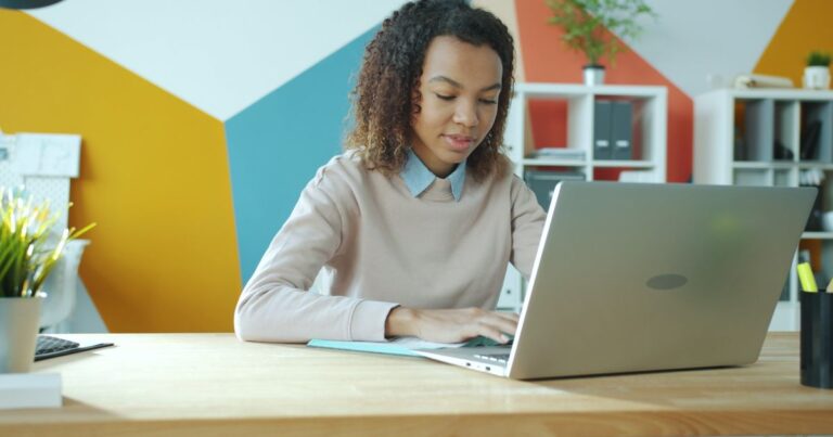 Page carrière qui convertit : une jeune candidate consulte une page carrière sur son ordinateur portable dans un bureau aux murs colorés